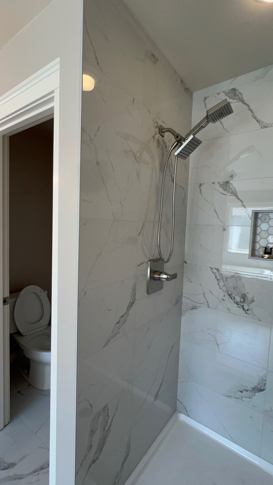 After: floor-to-ceiling large-format Calacatta marble-look porcelain shower with matching hex mosaic niche and brushed nickel fixtures in a Tacoma craftsman bathroom.