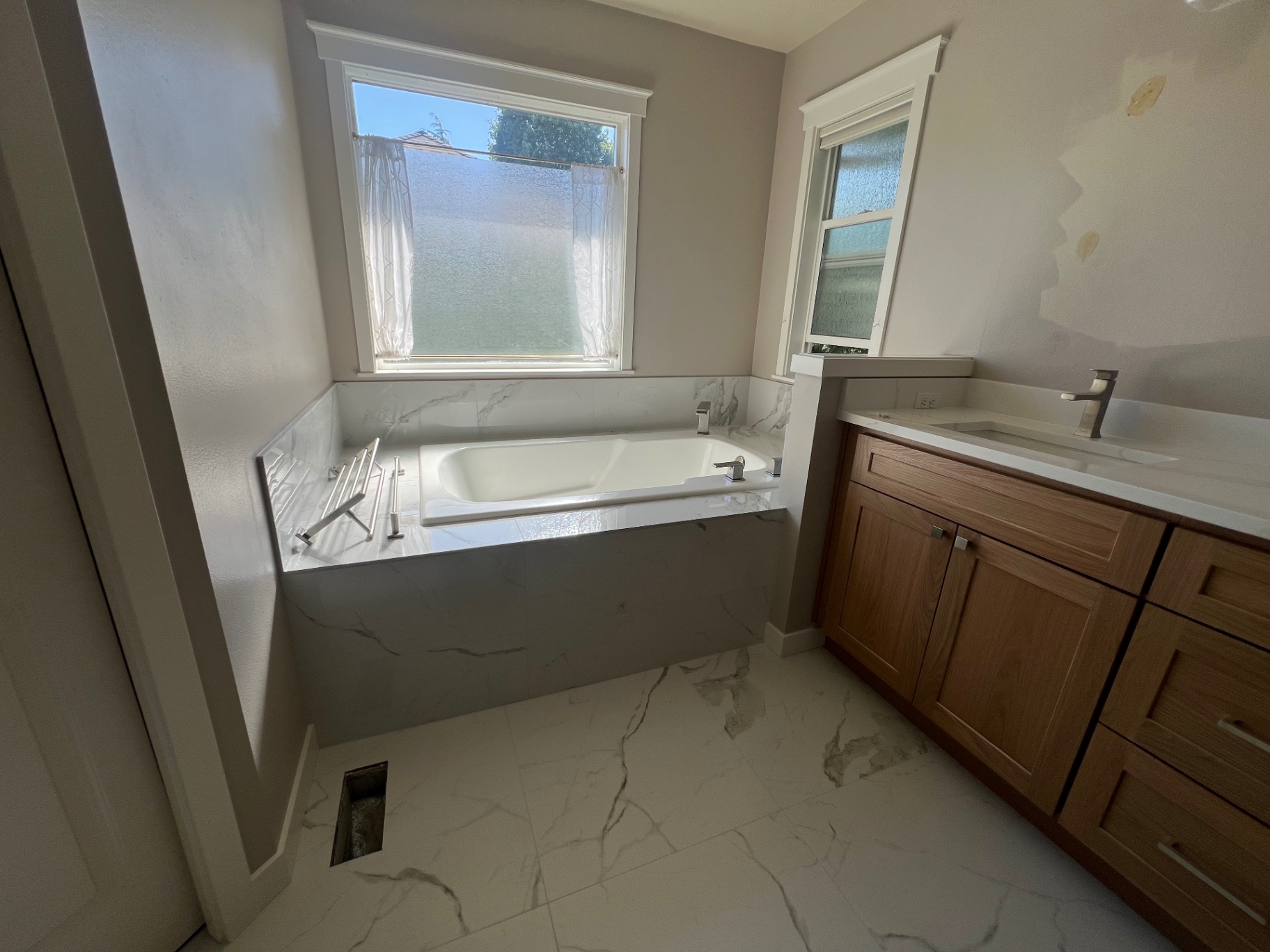 After: large-format marble-look porcelain tile tub surround and matching floor, white oak shaker vanity and quartz counter — completed by NorthWest Home Remodeling in West Seattle.