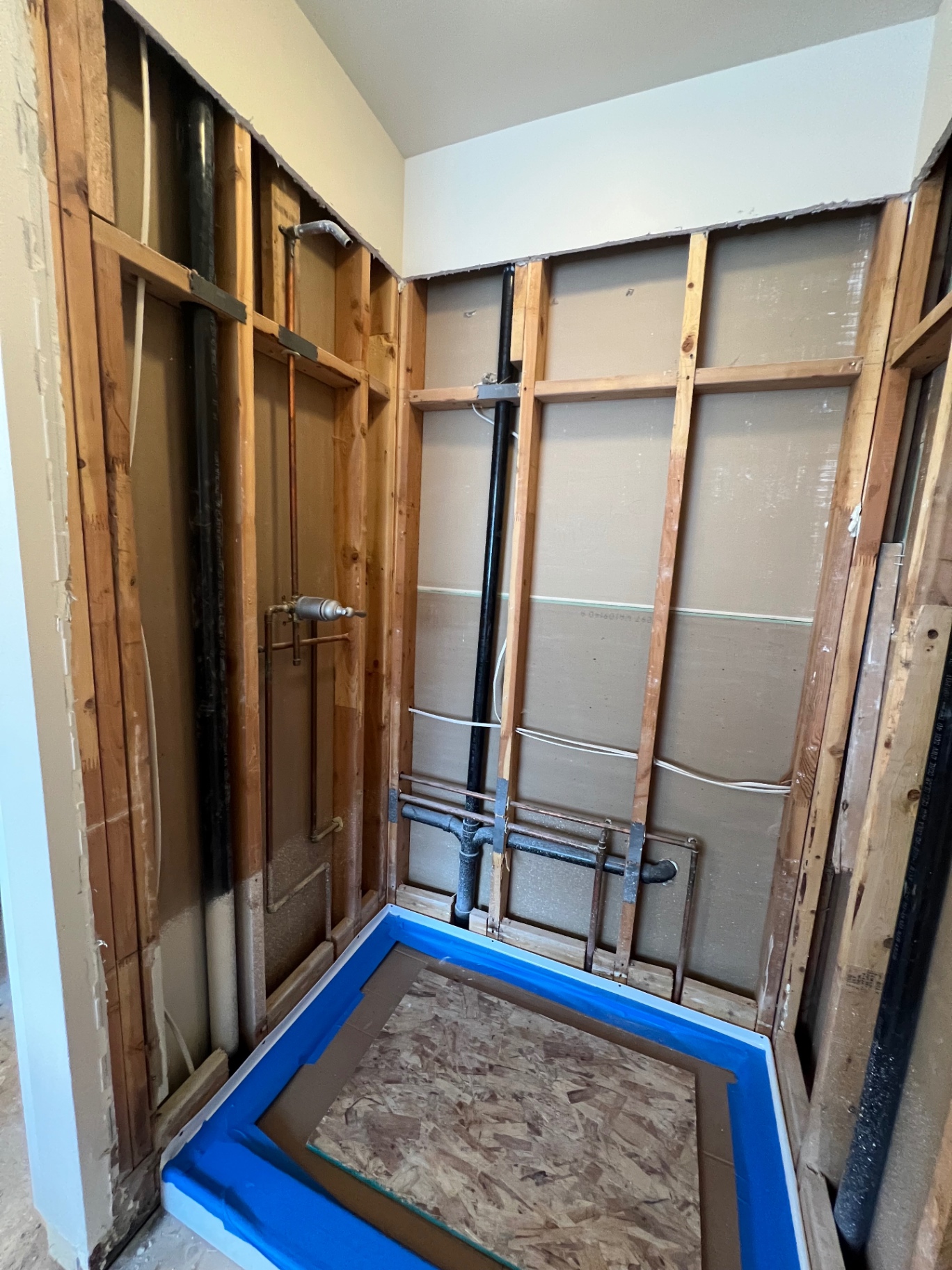 Before: shower stall demoed to studs with copper and PEX supply lines rerouted, new shower pan taped for waterproofing in a Tacoma bathroom remodel.