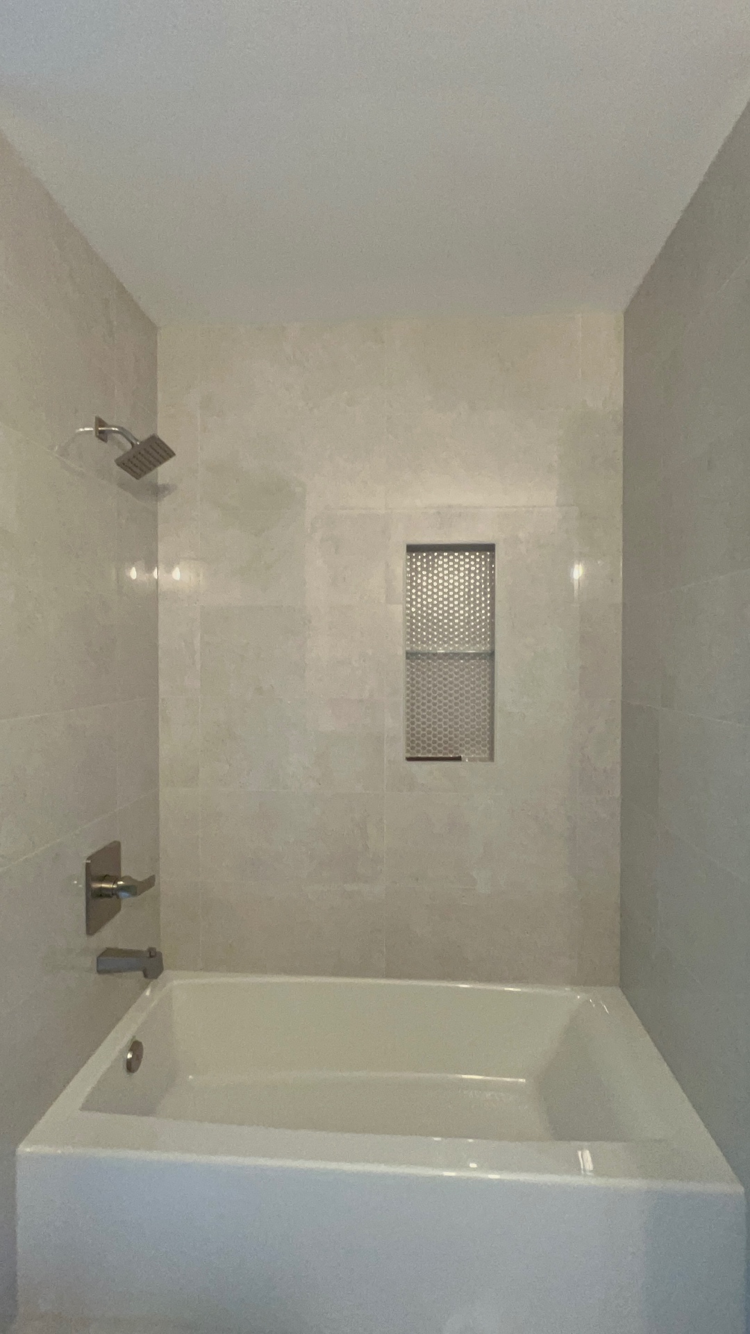 After: soft travertine-look 12×24 porcelain tub surround with a stainless honeycomb-mosaic recessed niche and satin nickel trim — finished by NorthWest Home Remodeling in Kent.