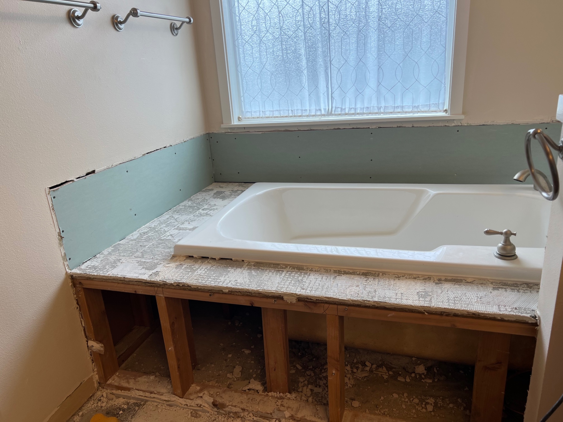 Before: dated drop-in tub with tile deck removed, exposed studs and green moisture-board backing in a West Seattle master bathroom before tile installation.